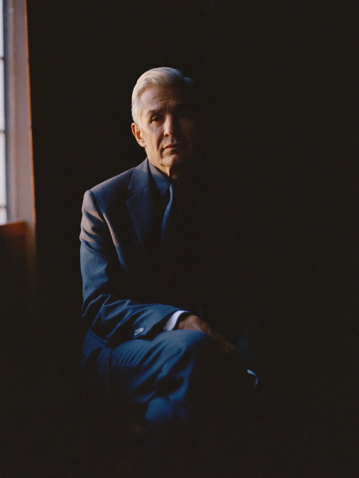 Studio portrait of a silver-haired attorney in a charcoal suit, seated in low window light