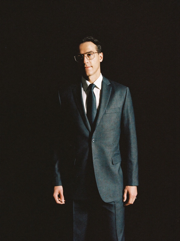 Studio portrait of an attorney with wire-frame glasses in a charcoal suit, lit from the left